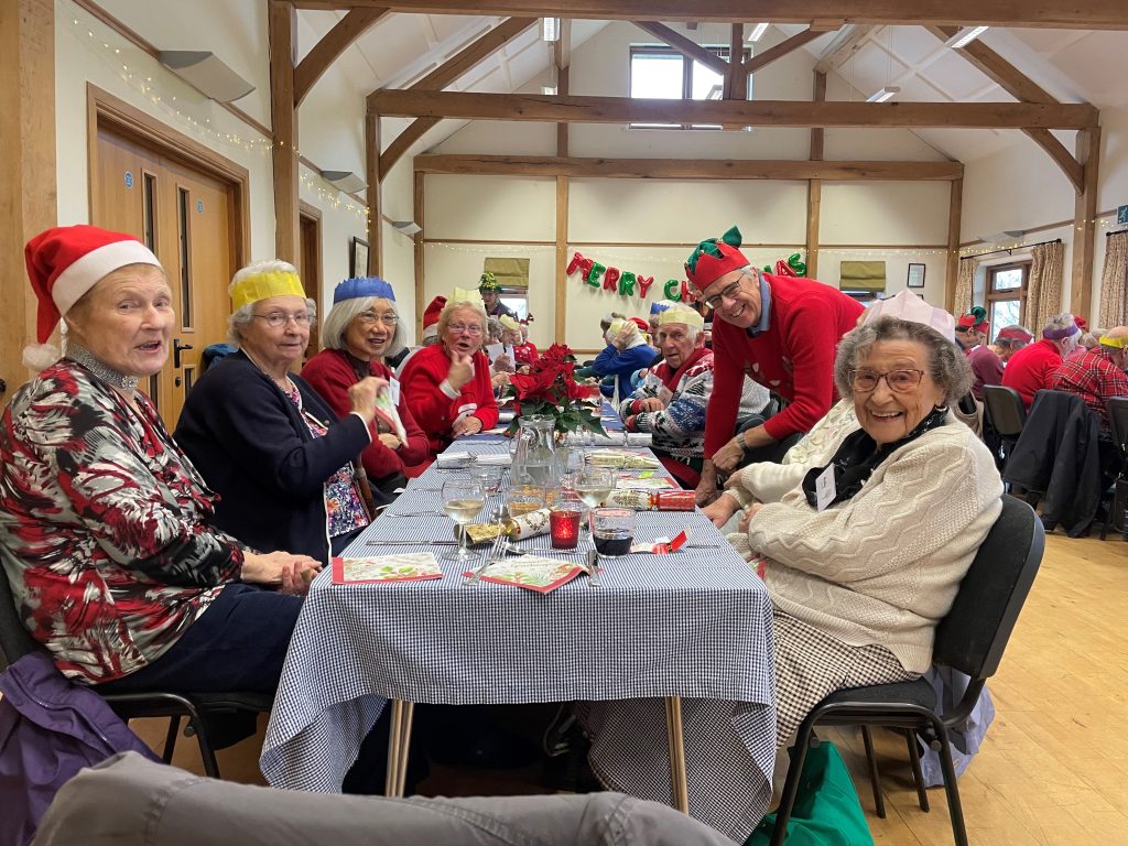 A group of older ladies sat at a table ready to eat a Christmas dinner. 