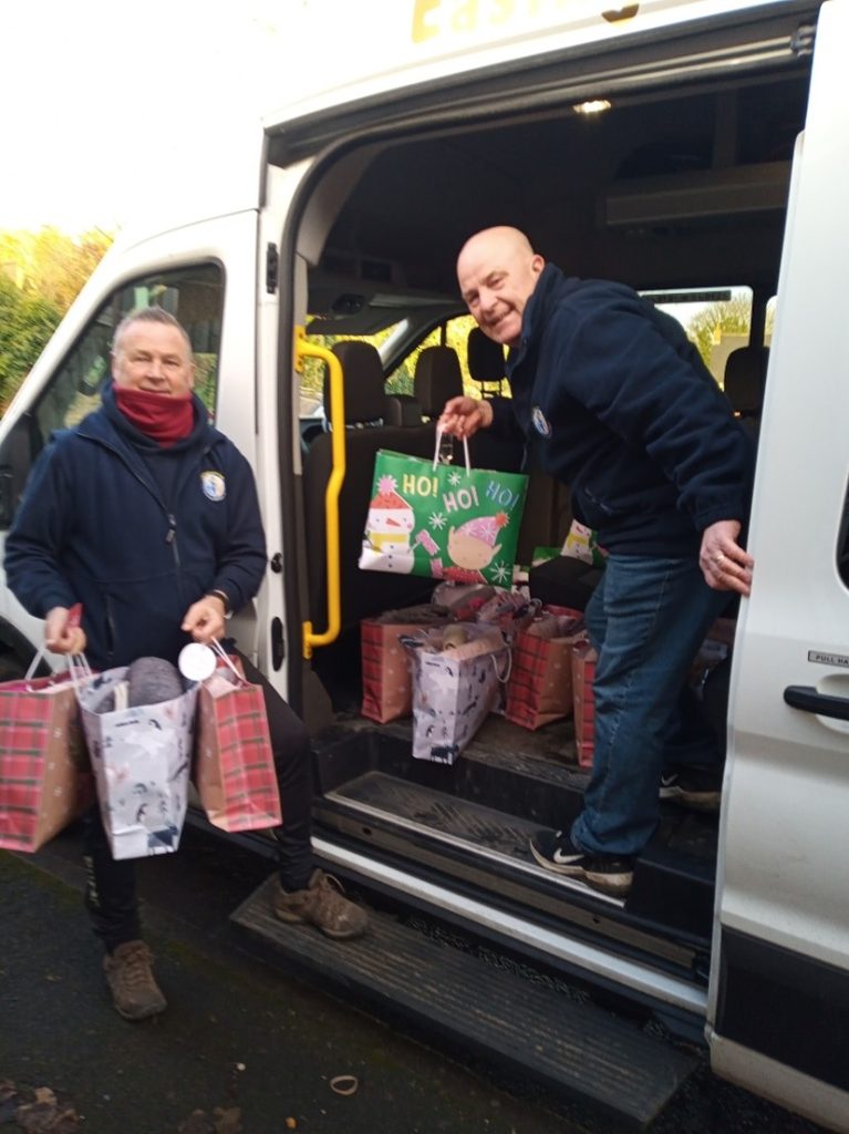 Two male volunteers unloading bags of Christmas gifts from a minibus